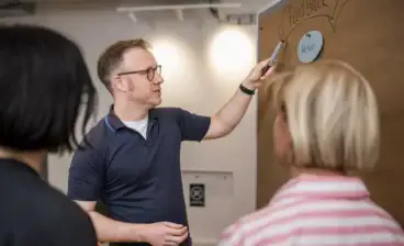 Mann erklärt Neurodiversität auf Whiteboard vor Gruppe.